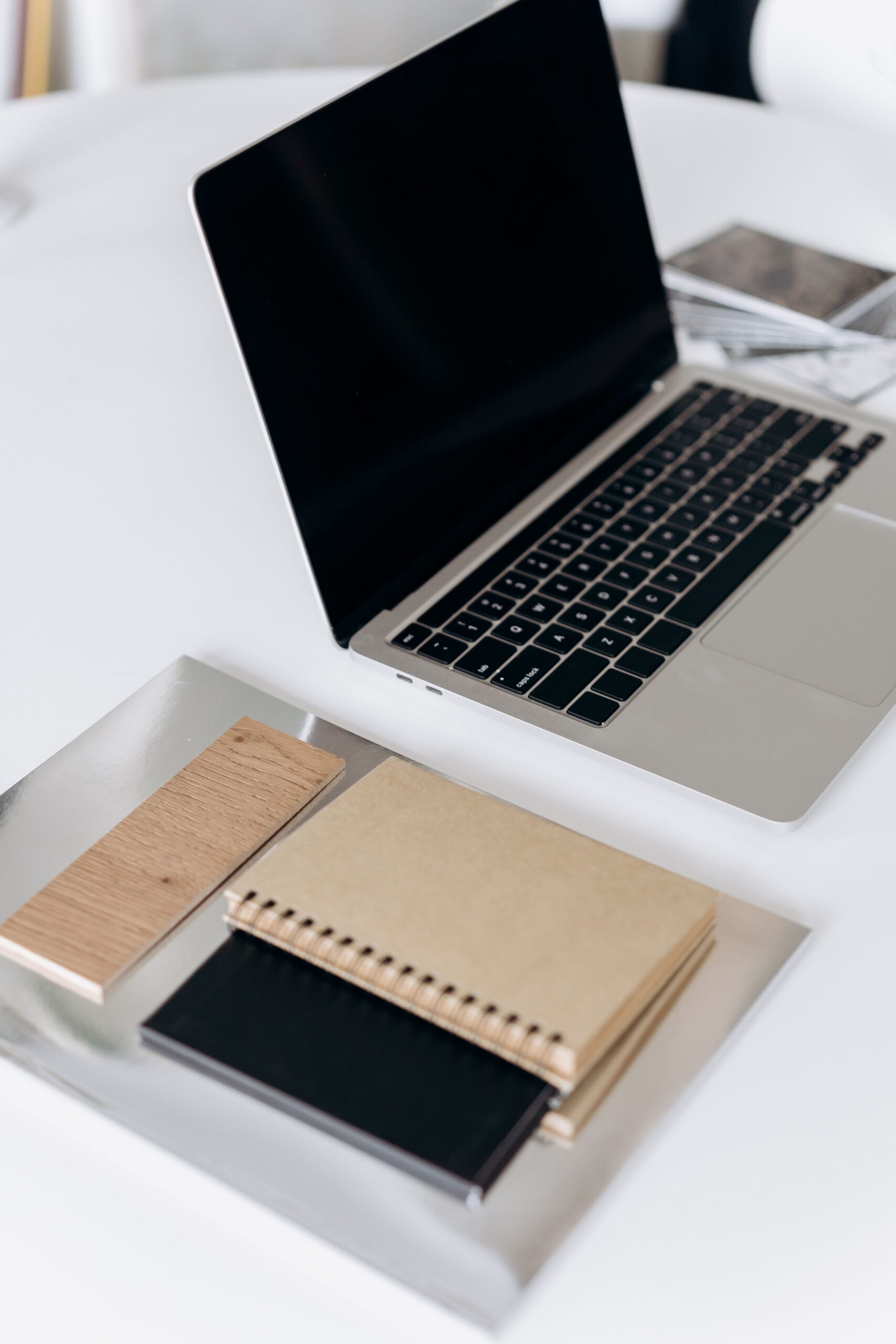 A clean and organized workspace with an open laptop and notebooks on a white table.